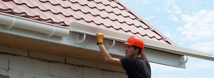 Monteur plaatst een nieuwe kunststof dakgoot onder een schuin pannendak tijdens dakgoot vervanging.