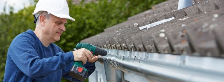 Een vakman monteert een nieuwe dakgoot met behulp van een accuboormachine.